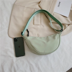 Flat lay of a light green nylon crescent crossbody bag with an adjustable strap on fabric