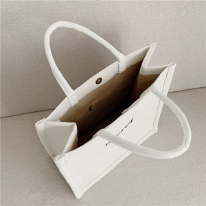 Detail of white canvas tote bag featuring khaki lining, zip pocket and magnetic closure