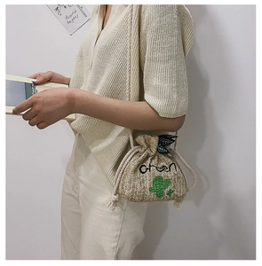 Detail of straw bucket bag with Green lettering and embroidered cactus on beige texture