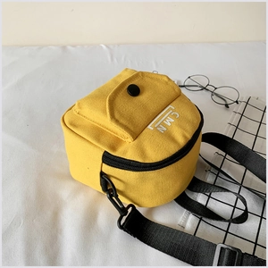Détail du sac bandoulière en toile jaune avec logo CMN sur fond de nappe blanche