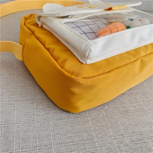 Close-up of small yellow canvas crossbody bag featuring a clear PVC window and bunny decor