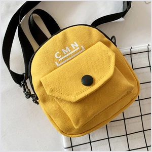 Détail d'un mini sac bandoulière en toile jaune avec imprimé CMN blanc et fermoir noir