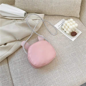 Detail of pink child crossbody bag with cute rabbit ears and woven rope strap on a sofa