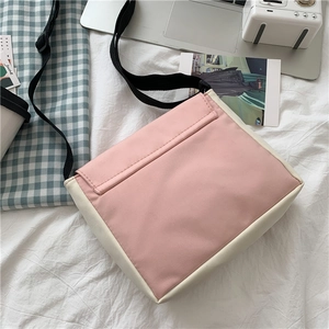 Close-up of pink and beige canvas crossbody bag with back compartment on white sheets