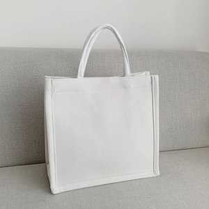 Minimalist white canvas tote bag with large capacity shown on a grey fabric sofa