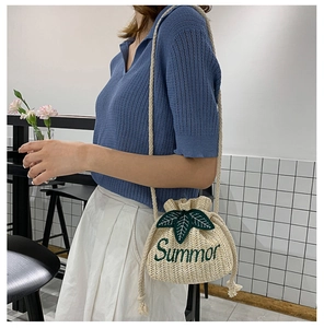 Detailed shot of beige straw bucket bag featuring green Summer embroidery and drawstring
