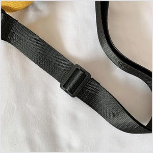 Détail de la bandoulière réglable en nylon noir avec boucle sur un sac en toile jaune