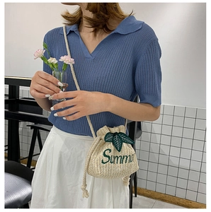 Detail of straw bucket bag featuring green Summer embroidery and leaf accent