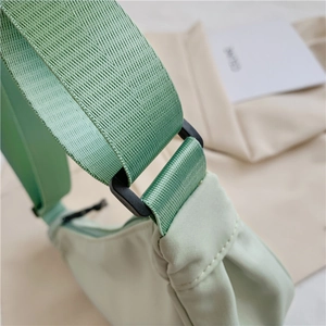 Detail of wide woven strap and black plastic buckle on mint green nylon crescent bag