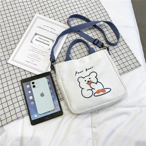 Detailed overhead shot of the white canvas bag with bear print and blue straps on grid cloth
