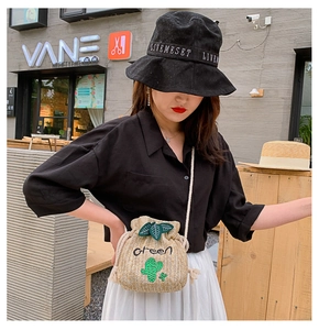 Detail of straw bucket bag with cactus embroidery and woven shoulder strap on model