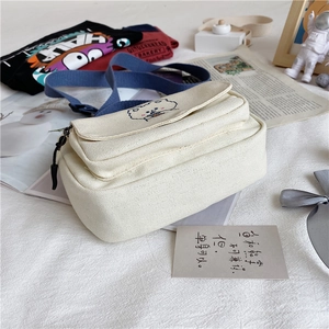 Close-up of cute bear embroidery and adjustable blue strap on a beige canvas bag
