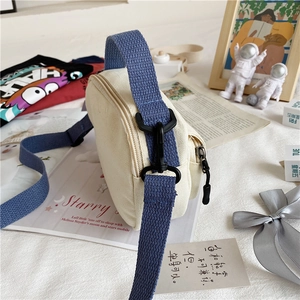Detail of canvas shoulder bag side featuring blue woven strap and black plastic hook