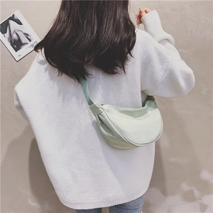 Close-up of a mint green nylon crescent bag worn crossbody over a white sweater