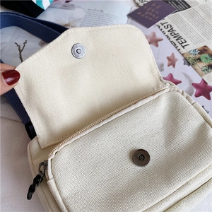 Close-up of cream canvas messenger bag showing the magnetic buckle and blue strap