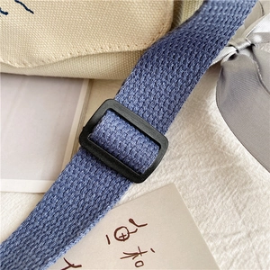 Detail of adjustable blue woven strap and black buckle on canvas messenger bag