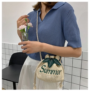 Detail of straw bucket bag featuring green Summer embroidery and crossbody rope strap