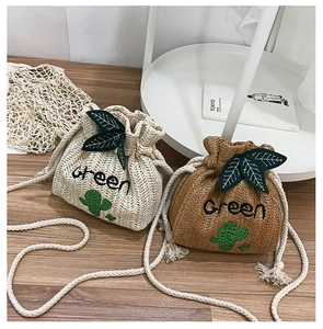 Detail of straw bucket bags with cactus embroidery and drawstring closure on wood surface