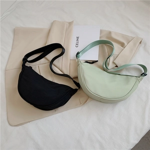 Close-up of black and light green nylon crescent bags with adjustable straps on soft fabric