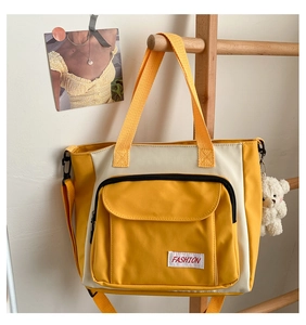 Detail of yellow and white canvas tote bag with large front pocket and plush bear charm