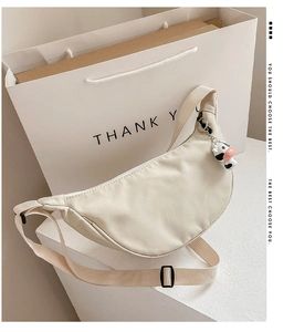 Close-up of beige nylon crescent bag with cow-shaped charm and adjustable shoulder strap