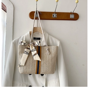Detail of woven straw tote bag with colored stripes, rope handle and silk scarf accessory
