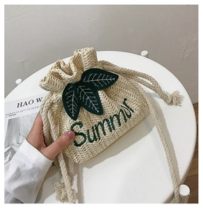Detail of handwoven straw bucket bag featuring green leaf decor and Summer embroidery
