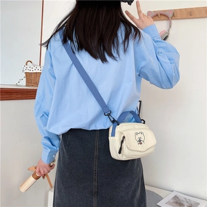 Detail of cute cream canvas crossbody bag with cartoon bear embroidery and blue strap