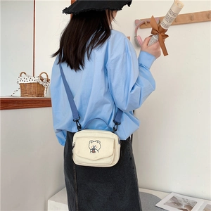 Detail of cream canvas crossbody bag featuring a cute bear embroidery and blue strap