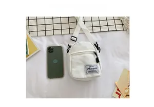 Detailed size comparison of a mini white canvas crossbody bag next to a smartphone