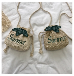 Detailed view of beige straw bucket bag featuring green Summer embroidery and leaf accents