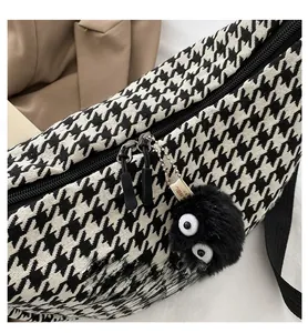 Detail of plaid crossbody bag featuring a black fuzzy coal sprite pendant and zipper