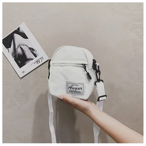 Detail of white canvas crossbody bag showing front zipper pocket and adjustable strap