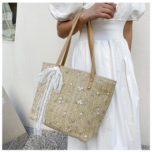 Detail of summer straw tote bag with delicate floral embroidery and white lace ribbon bow