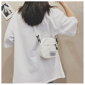 Rear view of a model wearing a mini white canvas crossbody bag with adjustable strap