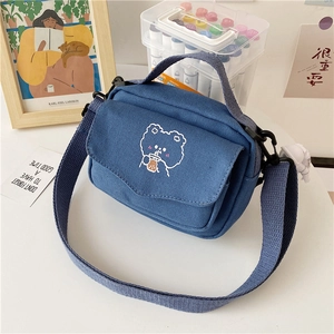 Detailed view of blue canvas bag featuring white embroidered bear and adjustable strap