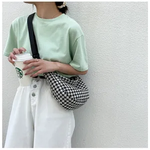 Detail shot of black and white houndstooth crossbody bag on a casual green outfit