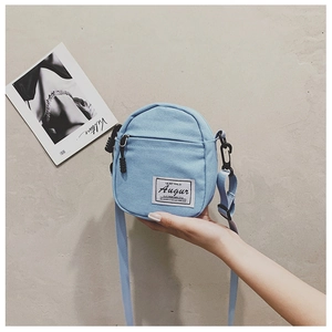 Detail of light blue canvas crossbody bag showing texture, woven label and zipper pocket