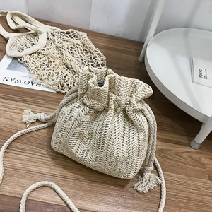 Minimalist straw bucket bag with drawstring closure and woven shoulder strap on a wooden floor
