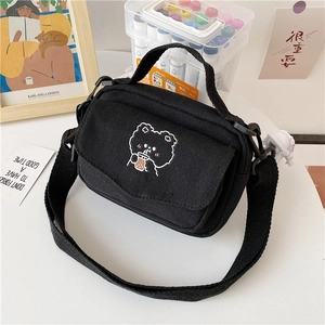 Detail of black canvas crossbody bag featuring a cute cartoon bear embroidery on table