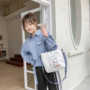 Close-up of white canvas shoulder bag featuring a cute cartoon bear and blue strap