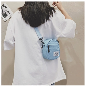 Detail of light blue mini canvas crossbody bag with adjustable strap and brand logo