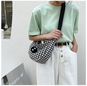 Detail of checkered half-moon crossbody bag with plush charm on casual outfit
