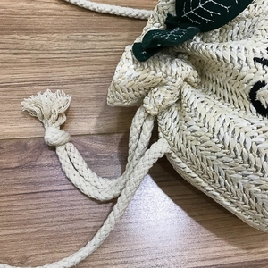 Handmade woven straw bucket bag with green leaf accents and drawstring closure