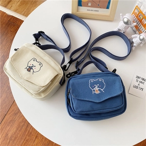 Detail of cream and navy canvas bags with bear embroidery and adjustable straps