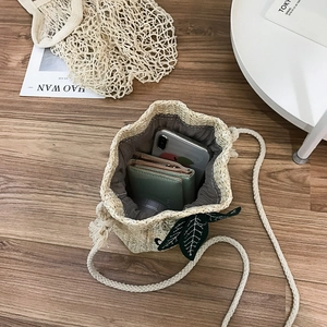 Handwoven beige straw bucket bag with green leaf charm and daily essentials inside