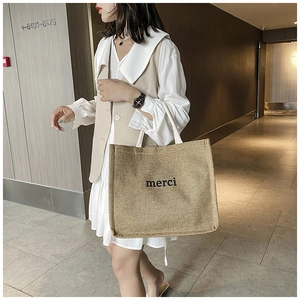 Detail of canvas tote bag with black merci print and neutral linen fabric texture