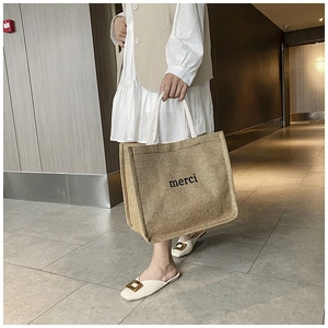 Detailed texture of natural jute tote bag with merci print and cream woven handles