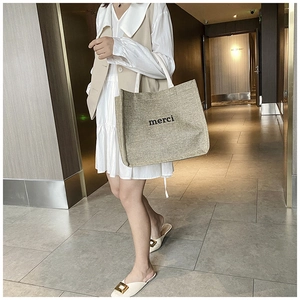 Detailed view of merci print on beige canvas tote bag with rustic woven texture