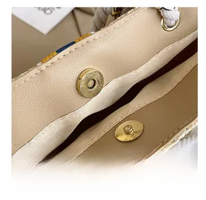 Close-up of golden magnetic buckle on beige woven tote with leather trim and cotton rope handle